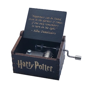 May include: A dark wooden Harry Potter music box with the quote "Happiness can be found, even in the darkest of times, if one only remembers to turn on the light." The box has a crank and a visible internal mechanism.