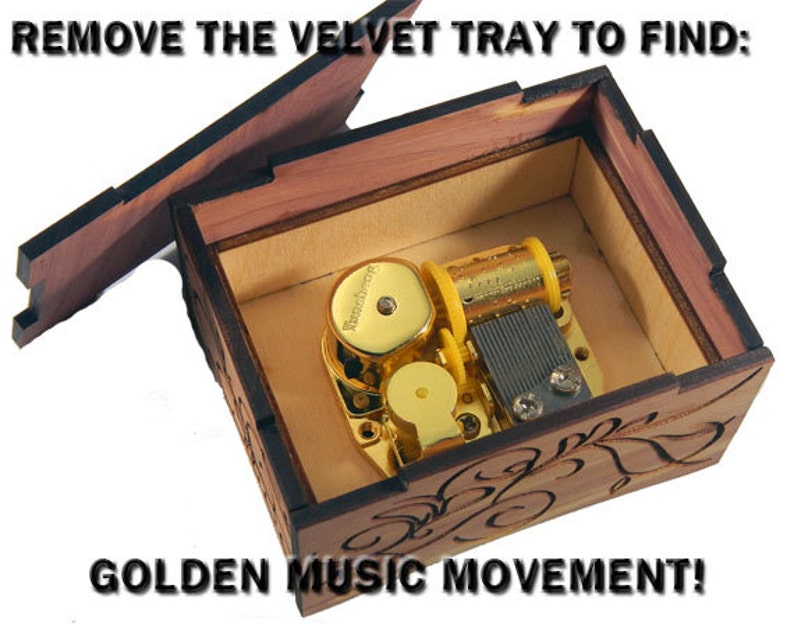 May include: A wooden music box with a hinged lid open, revealing a gold-colored music movement inside. The box has a carved floral design and the text "REMOVE THE VELVET TRAY TO FIND: GOLDEN MUSIC MOVEMENT!" is printed on the lid.