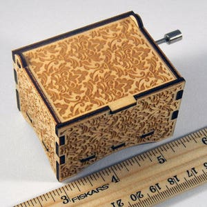 May include: A wooden music box with a floral pattern on the top and sides. The box is closed and has a metal winding key on the side.