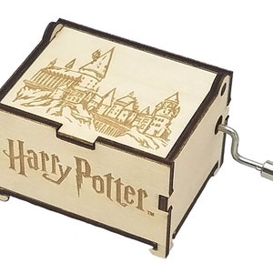 May include: A wooden music box with a hand-crank on the side. The top of the box features a laser-engraved image of Hogwarts Castle from the Harry Potter series. The text "Harry Potter" is engraved on the front of the box.