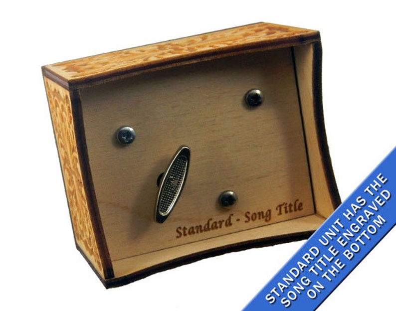 May include: A wooden music box with a light brown finish and a decorative engraved design. The box has a crank on the side and a small metal plate on the front that says "Standard - Song Title".