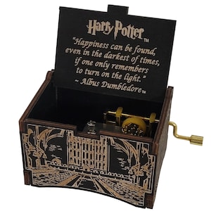 May include: A dark brown wooden music box with a gold-colored hand crank. The lid interior features the Harry Potter logo and the quote: Happiness can be found, even in the darkest of times, if one only remembers to turn on the light. ~ Albus Dumbledore.