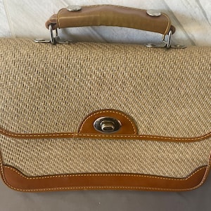 May include: A vintage handbag with a woven beige body and brown leather trim. The bag features a top handle, a metal clasp closure, and metal hardware. The bag's design is rectangular with rounded corners.