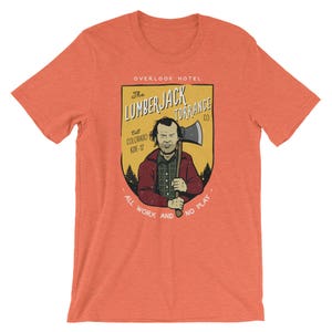 Może przedstawiać: Pomarańczowy T-shirt z grafiką w stylu vintage przedstawiającą mężczyznę trzymającego siekierę. Grafika zawiera napis "The Lumberjack Torrance Co." i "All work and no play".