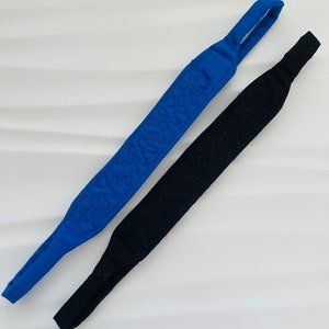 Peut inclure: Deux sangles pour lunettes, l'une bleue et l'autre noire. Les deux sangles ont une texture matelassée et sont en tissu.