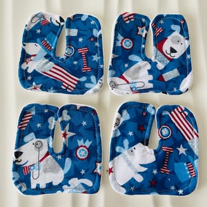 Peut inclure: Quatre lettres en tissu formant le mot "USA" en bleu avec des étoiles blanches, des rayures rouges et blanches, et des chiens blancs avec des accents rouges, blancs et bleus.