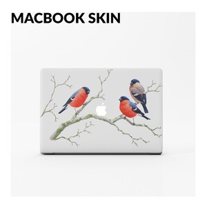 May include: A white MacBook laptop with a skin featuring a wintery scene with three red-breasted robins perched on a branch. The skin is a digital design with a white background and a subtle gray branch.