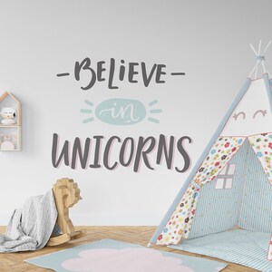 May include: A white wall with a blue and white teepee tent, a rocking horse, a fluffy rug, and a wall decal that says "Believe in Unicorns".