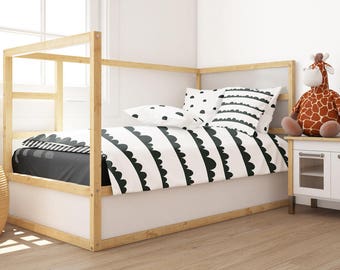 Puede incluir: Un marco de cama de madera blanca con un juego de ropa de cama de patrones blanco y negro. La cama está en una habitación con una pared blanca y un suelo de madera. Hay un juguete de peluche de jirafa en un gabinete blanco con una parte superior de madera.