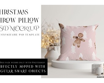 May include: A pink throw pillow with a white gingerbread man and pine tree pattern. The pillow is on a white pedestal against a white background.