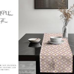 May include: A pink and gold table runner with a geometric pattern. The runner is on a black table with a white bowl and a vase with dried flowers.