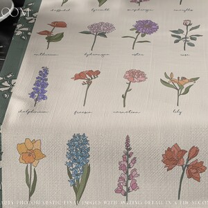 May include: A beige linen table runner with a green border features a floral design with the names of different flowers printed below each illustration. The flowers include daffodil, hyacinth, sweet pea, myrtle, anemone, delphinium, freesia, carnation, lily, orchid, narcissus, hydrangea, aster, rose, and more.