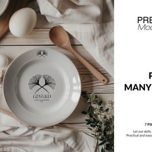 May include: A white ceramic plate with a black and white ginkgo leaf design and the text "GINGKO GOODS AND BRANDING CO.". The plate is on a wooden surface with a white cloth and a wooden spoon.