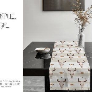 May include: A beige table runner with a repeating pattern of brown bull skulls and geometric designs. The runner is on a black table with a white bowl and a vase of dried flowers.