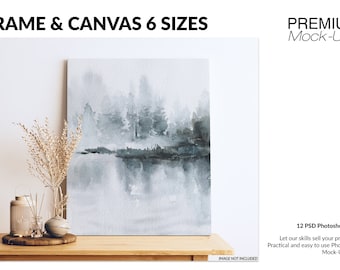 May include: A framed canvas print of a watercolor painting depicting a misty forest scene with a reflection in the water. The canvas is displayed on a wooden table with decorative items, including a vase with dried flowers, a lantern, and a diffuser.