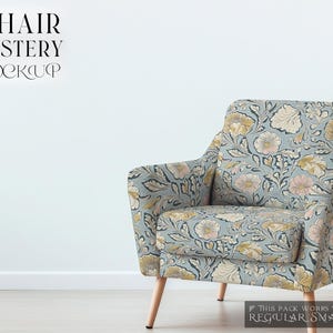 May include: A floral patterned armchair with a light blue background and beige and pink floral accents. The chair has wooden legs and is sitting on a white floor in front of a white wall.