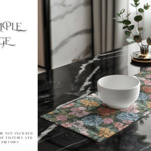 May include: A white ceramic bowl sits on a floral table runner with a green background. The runner has pink, yellow, and blue flowers. The table runner is on a black marble table.
