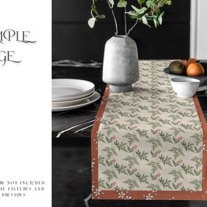 May include: A beige table runner with a green and red floral pattern. The runner has a rust-colored border with a white floral pattern. The runner is on a black table with a white plate and a vase with green leaves.