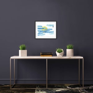 May include: A framed watercolour painting of a yellow sun behind blue and green clouds. The painting is hanging on a dark grey wall above a white marble console table with two potted plants.