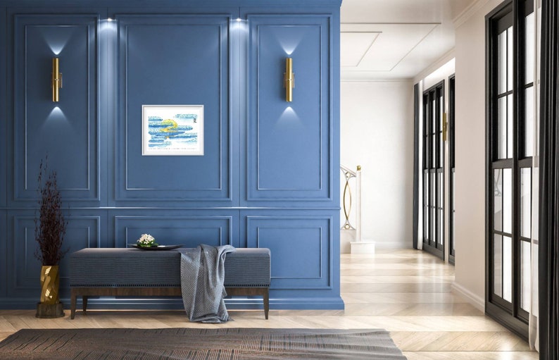 May include: A blue wall with white trim and gold wall lights. A framed abstract painting with blue and yellow paint is hanging on the wall. A bench with a grey blanket is in front of the wall.