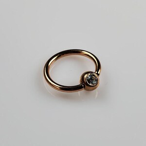 May include: A rose gold captive bead ring with a clear gem in the bead.