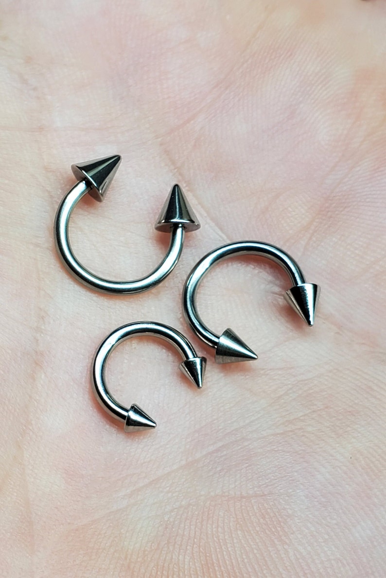 May include: Three silver-colored circular body piercing rings with pointed ends. The rings are of different sizes.