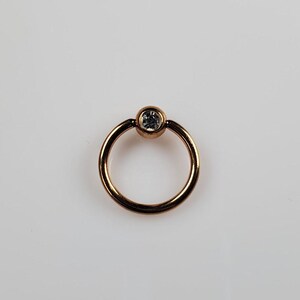 May include: A gold-toned circular ring with a clear gemstone in the center.