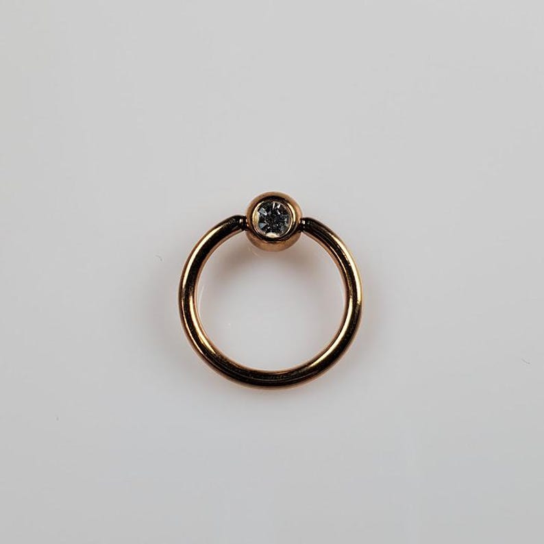 May include: A gold-toned circular ring with a clear gemstone in the center.
