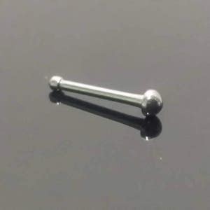 May include: A silver-colored nose stud with a straight bar and a ball on each end. The jewelry is shown against a dark, reflective surface. The nose stud is a simple, minimalist design.