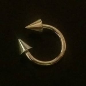 May include: A gold-toned circular body piercing with two pointed ends.
