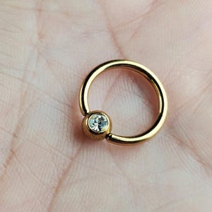 May include: Gold body jewelry with a clear gem in the center.