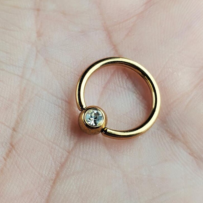May include: Gold body jewelry with a clear gem in the center.