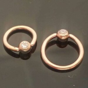 May include: Two gold-toned hoop earrings with a clear gemstone in the center of each hoop.