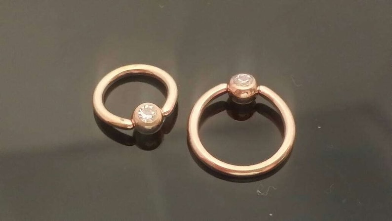 May include: Two gold-toned hoop earrings with a clear gemstone in the center of each hoop.