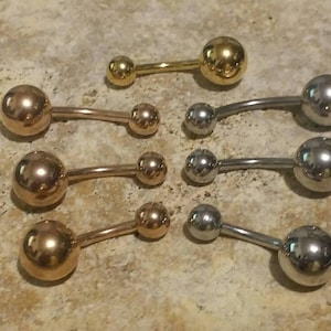 May include: A set of six belly button rings with different colored balls. The balls are gold, silver, and rose gold. The rings are made of metal.
