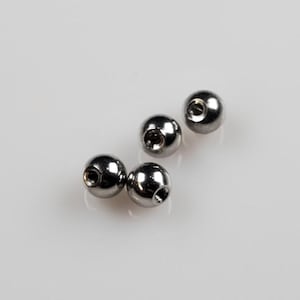 May include: Four shiny, silver-colored metal ball beads with a hole drilled through each. The beads are round and reflect light, creating highlights. The beads are likely for jewelry making or crafts.