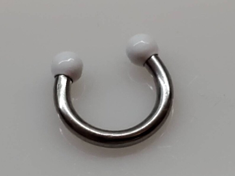 May include: A silver horseshoe-shaped barbell with white ball ends. The barbell is a type of body jewellery.