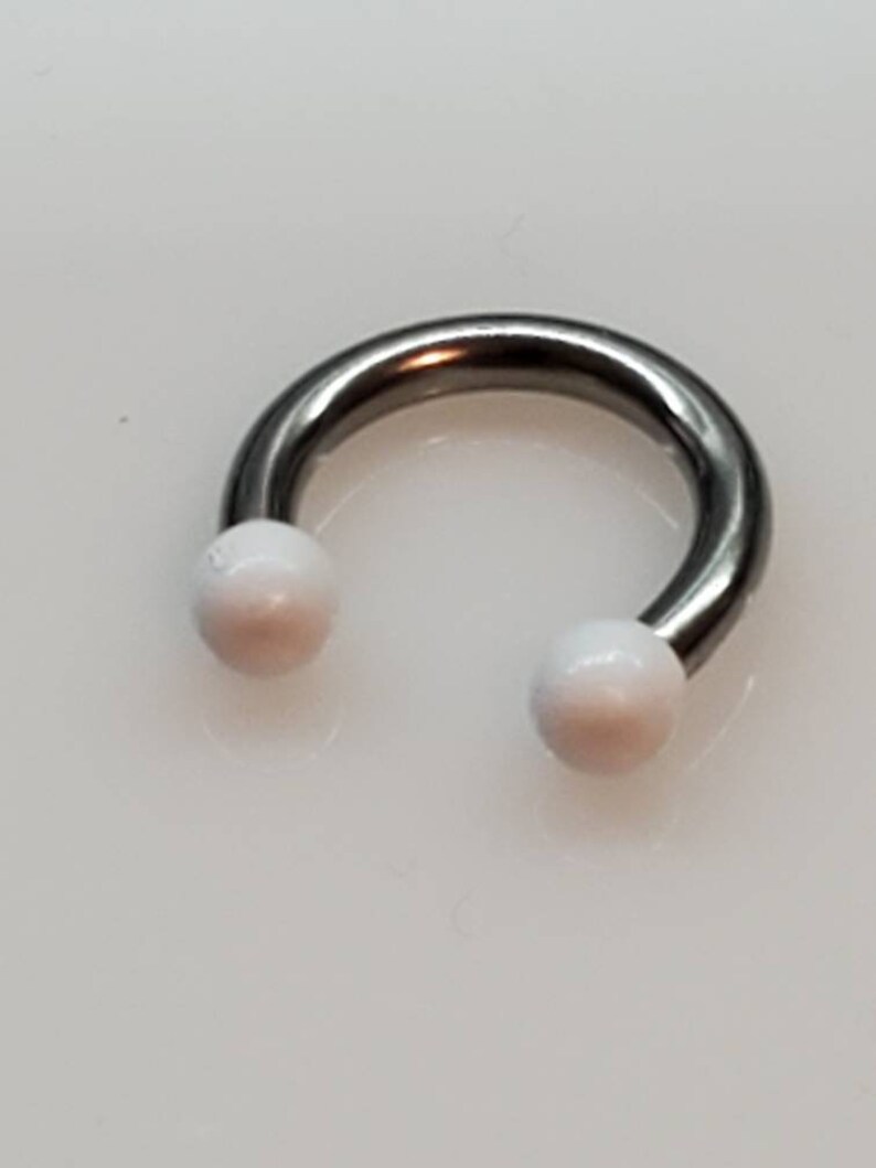 May include: A silver circular barbell with white balls on each end.