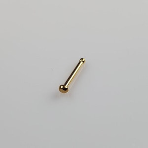 May include: A gold nose ring with a rounded end.