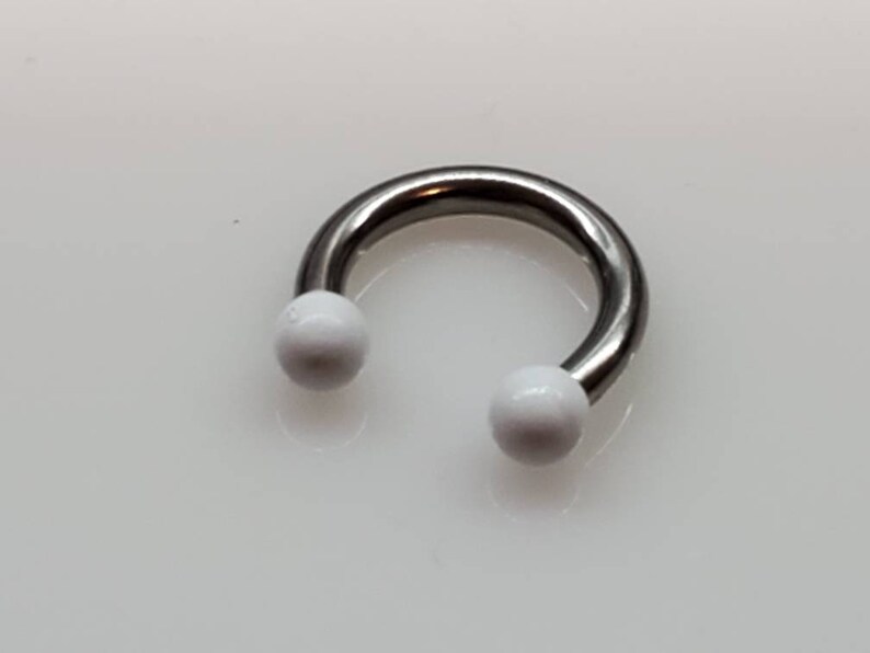 May include: A silver horseshoe-shaped body piercing with white balls on each end.