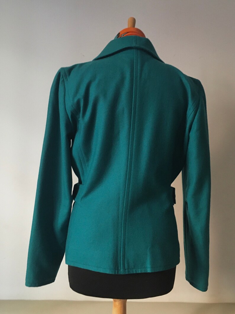May include: Teal blazer with long sleeves and a single button closure. The blazer has a fitted silhouette and a belt at the waist.