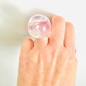 以下が含まれることがあります： 気泡のデザインが施された透明なガラスのリング。指につけられています。