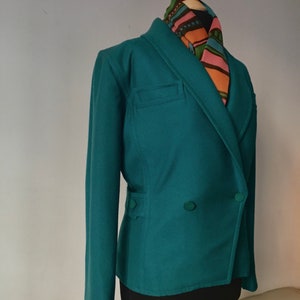 May include: A teal double-breasted blazer with a long sleeve and two buttons. The blazer has a pocket on the left side and is worn on a mannequin with a colorful patterned scarf.