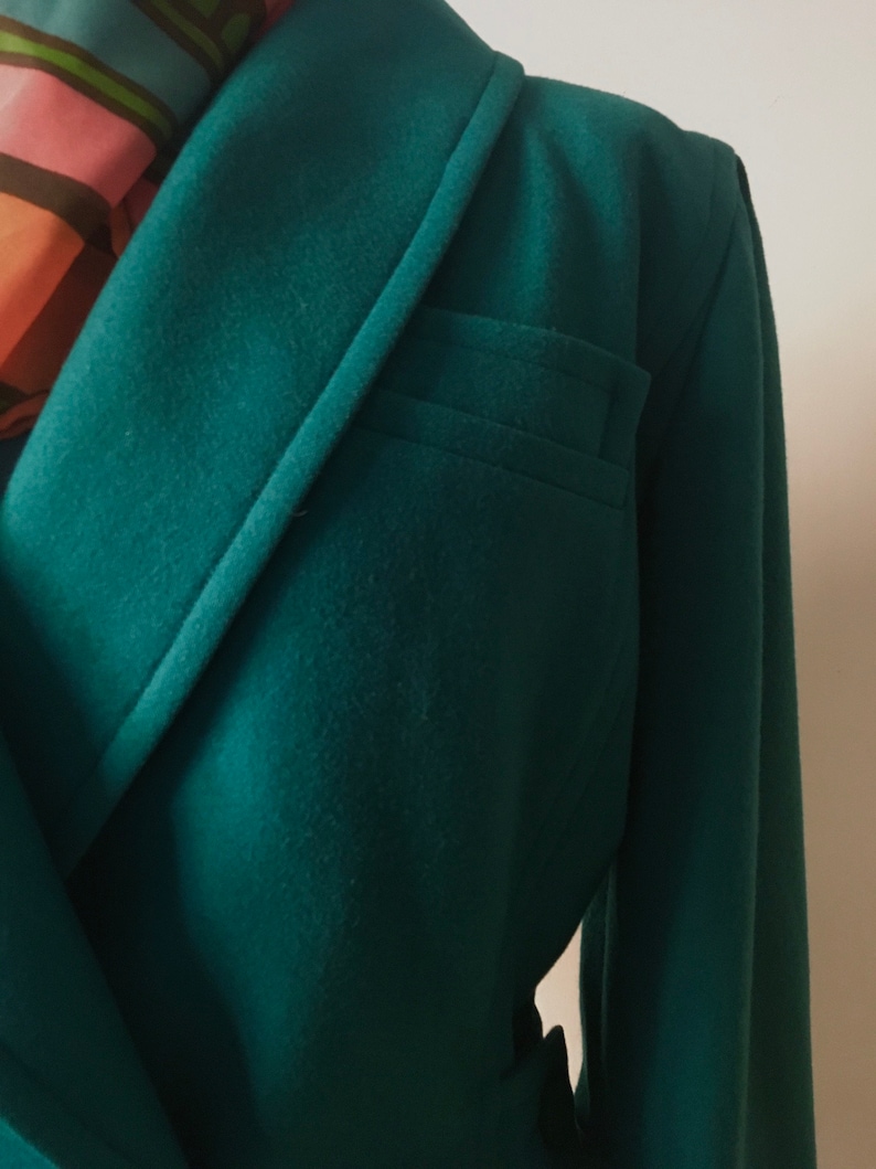 May include: A dark green wool blazer with a single button closure and a flap pocket on the left side. The blazer has a notched collar and long sleeves.