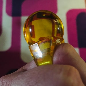 以下が含まれることがあります： 透明なファセットデザインの黄色いガラス製のリング。リングの側面には「MIR」という文字が刻まれています。