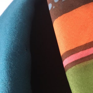 May include: Close-up of two fabric swatches. One is a solid teal blue and the other is a multi-colored striped fabric with brown, orange, pink, and green stripes.