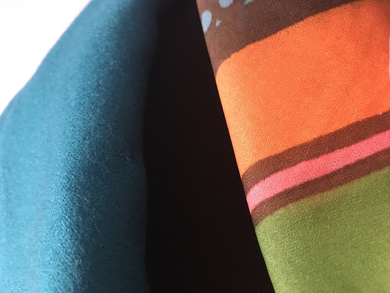 May include: Close-up of two fabric swatches. One is a solid teal blue and the other is a multi-colored striped fabric with brown, orange, pink, and green stripes.