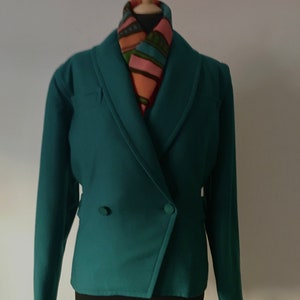 May include: A teal green blazer with a double breasted closure and long sleeves. The blazer has a shawl collar and is worn on a mannequin with a patterned scarf.