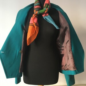 May include: A teal blue blazer with a colorful patterned scarf. The blazer has a brown lining and is open to show the lining.