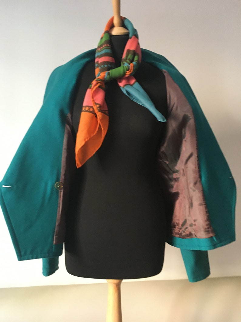 May include: A teal blue blazer with a colorful patterned scarf. The blazer has a brown lining and is open to show the lining.